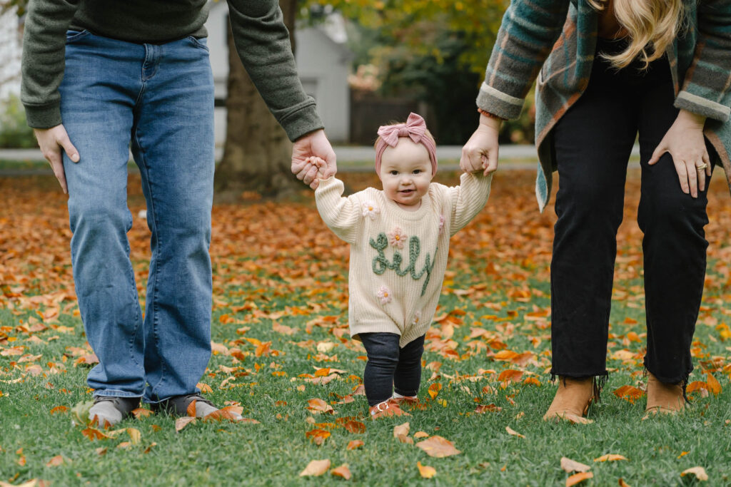 parents helping baby walk in the park during woodstock vermont fall family photo session