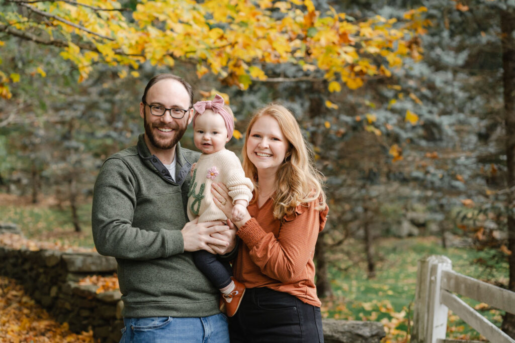 parents sitting on stone wall with baby during woodstock vermont fall family photo session
