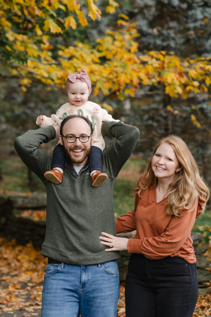 baby on father's shoulders with mom standing near during woodstock vermont fall family photo session