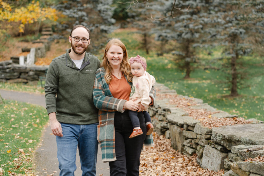 parents and baby walking along stone wall at faulkner park during woodstock vermont fall family photo session