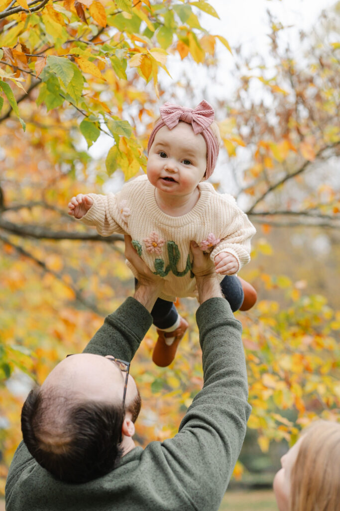 baby flying in the air with fall leaves in background during woodstock vermont fall family photo session