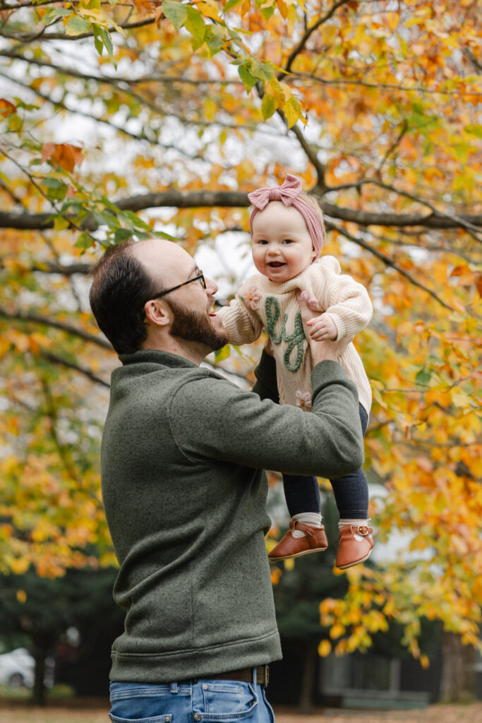 father holding baby up near foliage during woodstock vermont fall family photo session