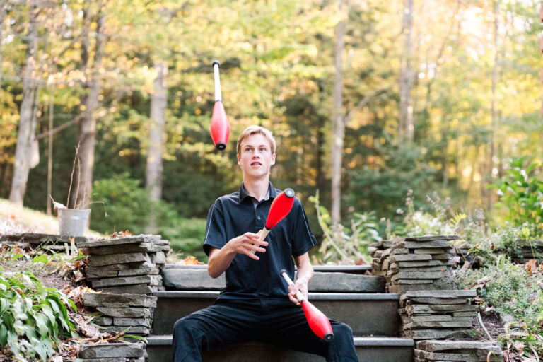 Senior boy juggling pins for high school senior portrait with fall foliage backdrop