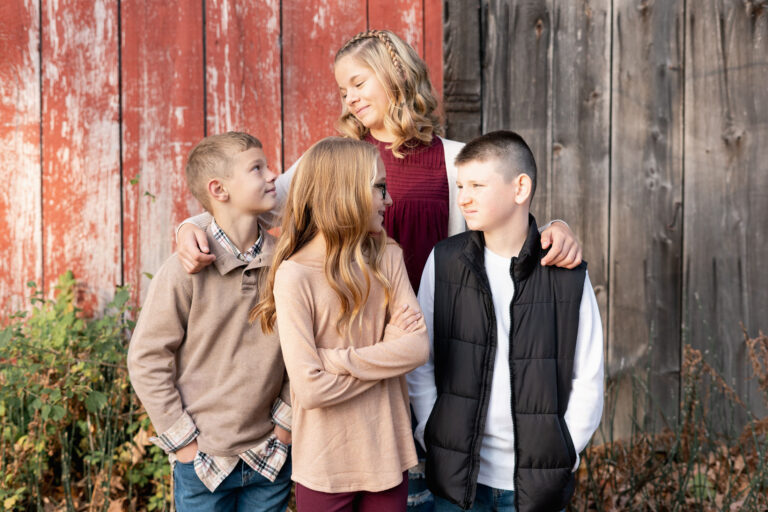 four young siblings standing together in front of barn