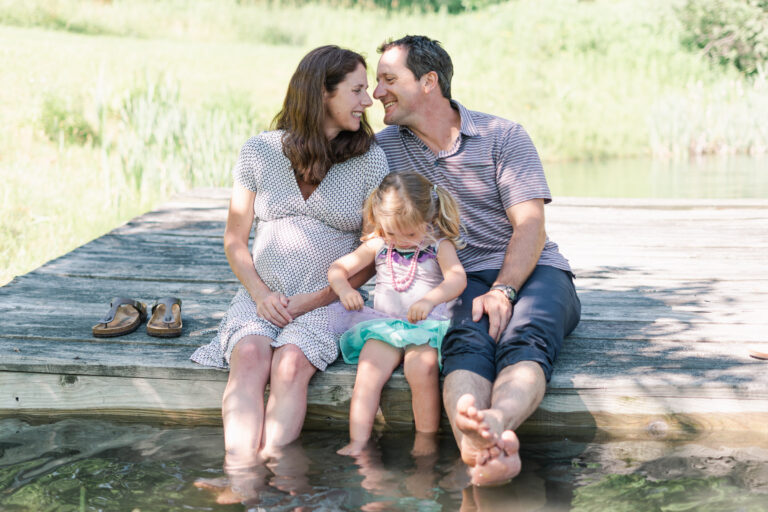 pregnant woman with family sitting on dock with toes in water