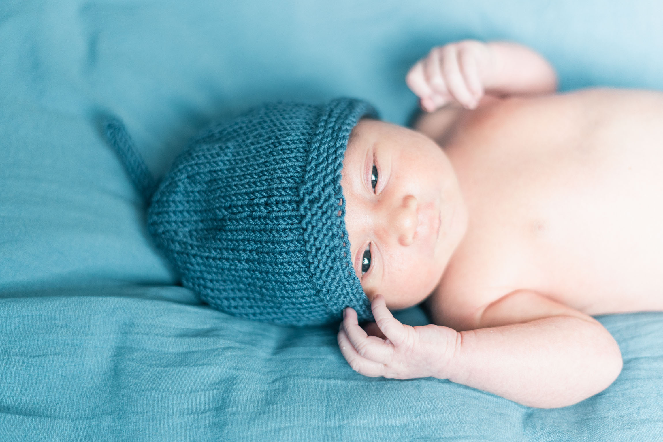 newborn wearing blue knit hat that matches bedspread