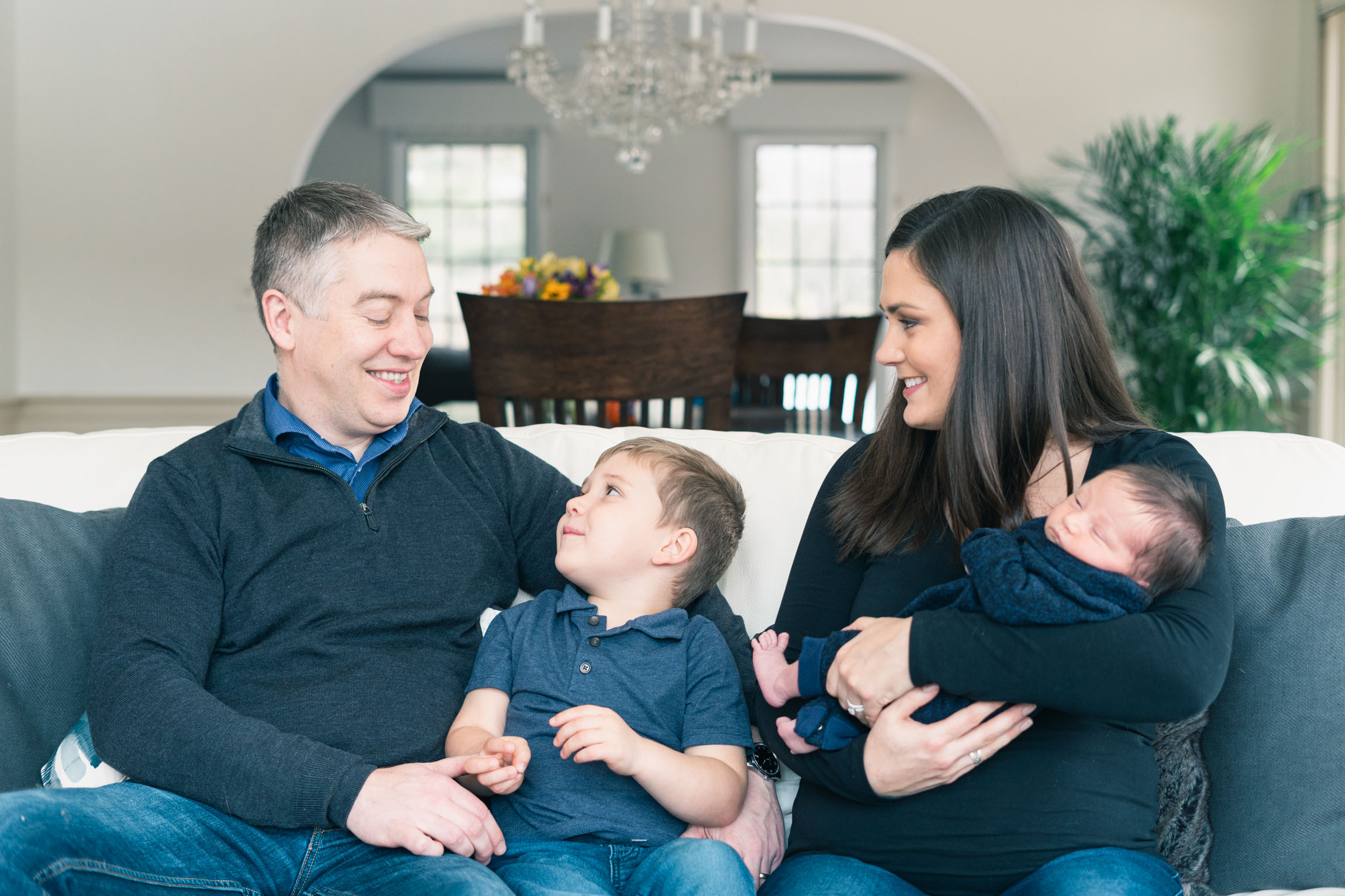 family sitting on couch, mother holding newborn father looking at son