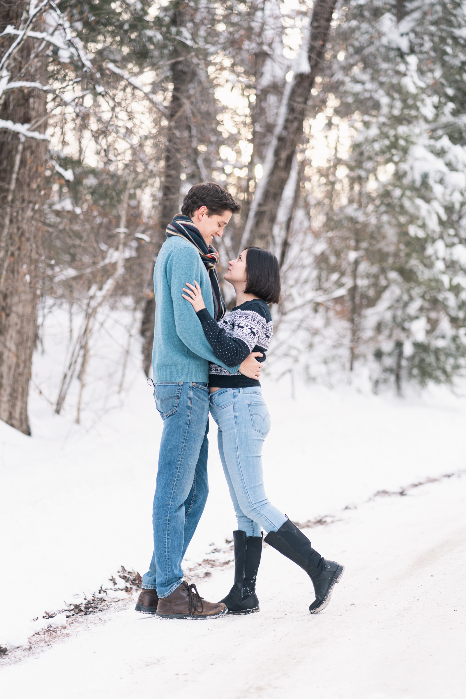 couple standing on snowy country road in New Hampshire with sun setting behind trees in background