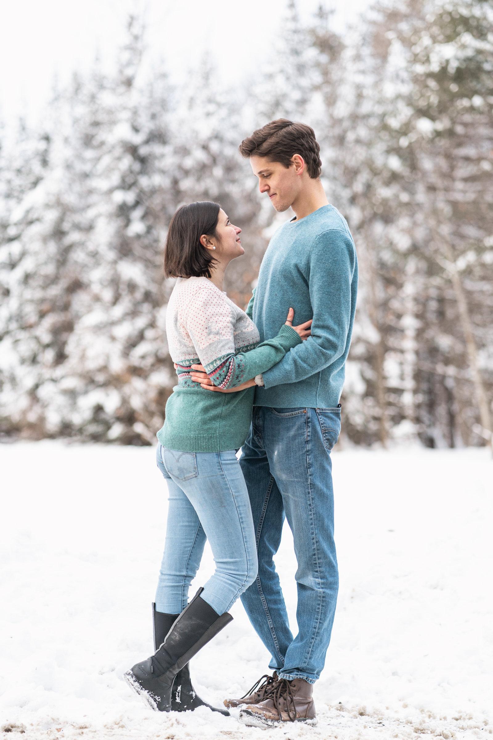 couple standing facing each other with snowy woods behind them