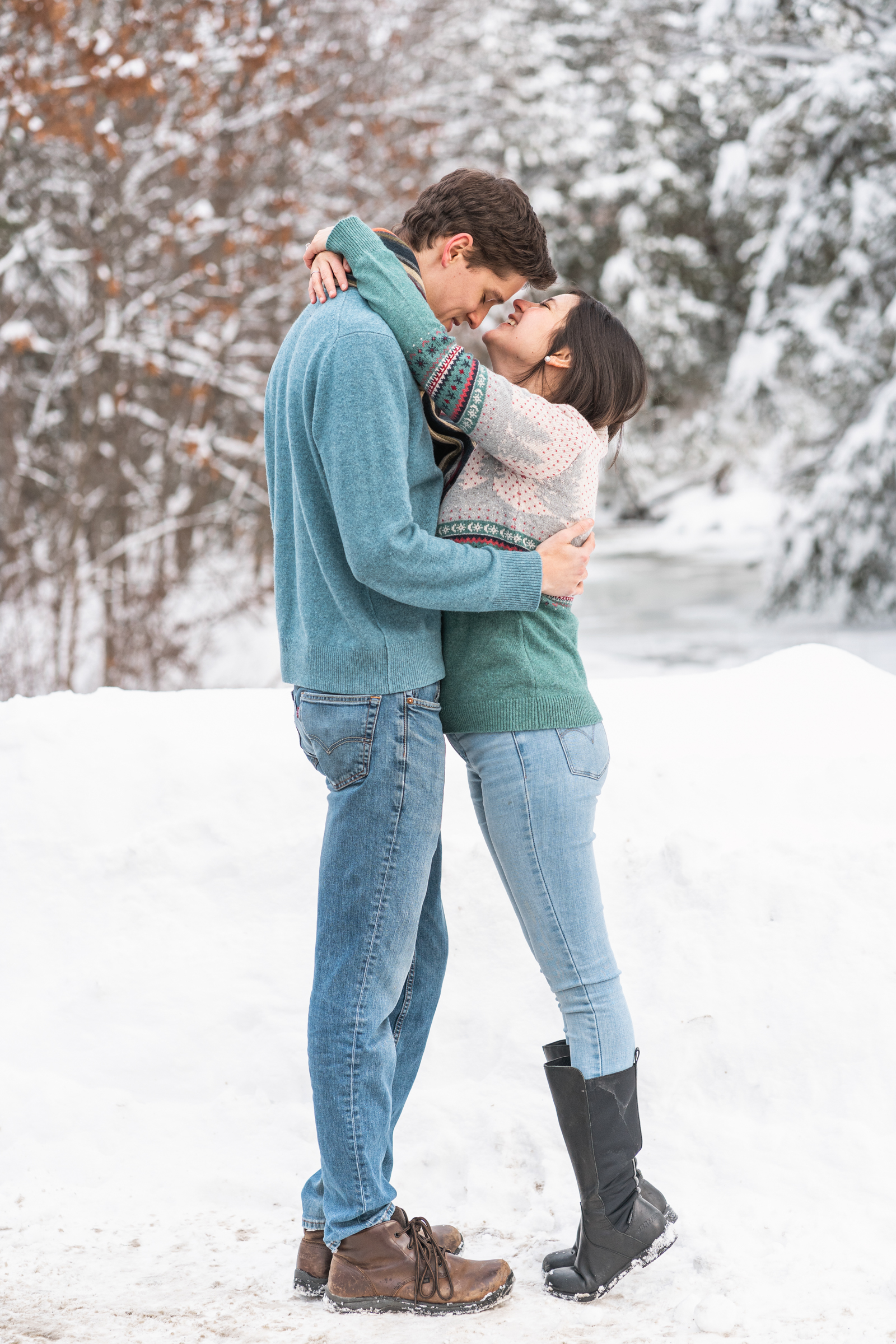 wife on tiptoes to kiss husband's forehead with snowy river in background