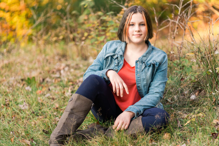portrait of young female sitting in grass with boots and denim jacket