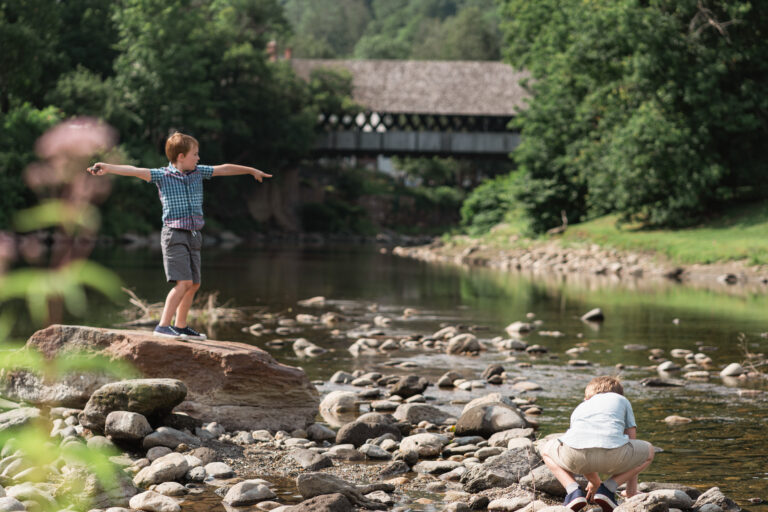 Boys playing at Outtauquechee River with Middle Covered Bridge in background, Woodstock, Vermont