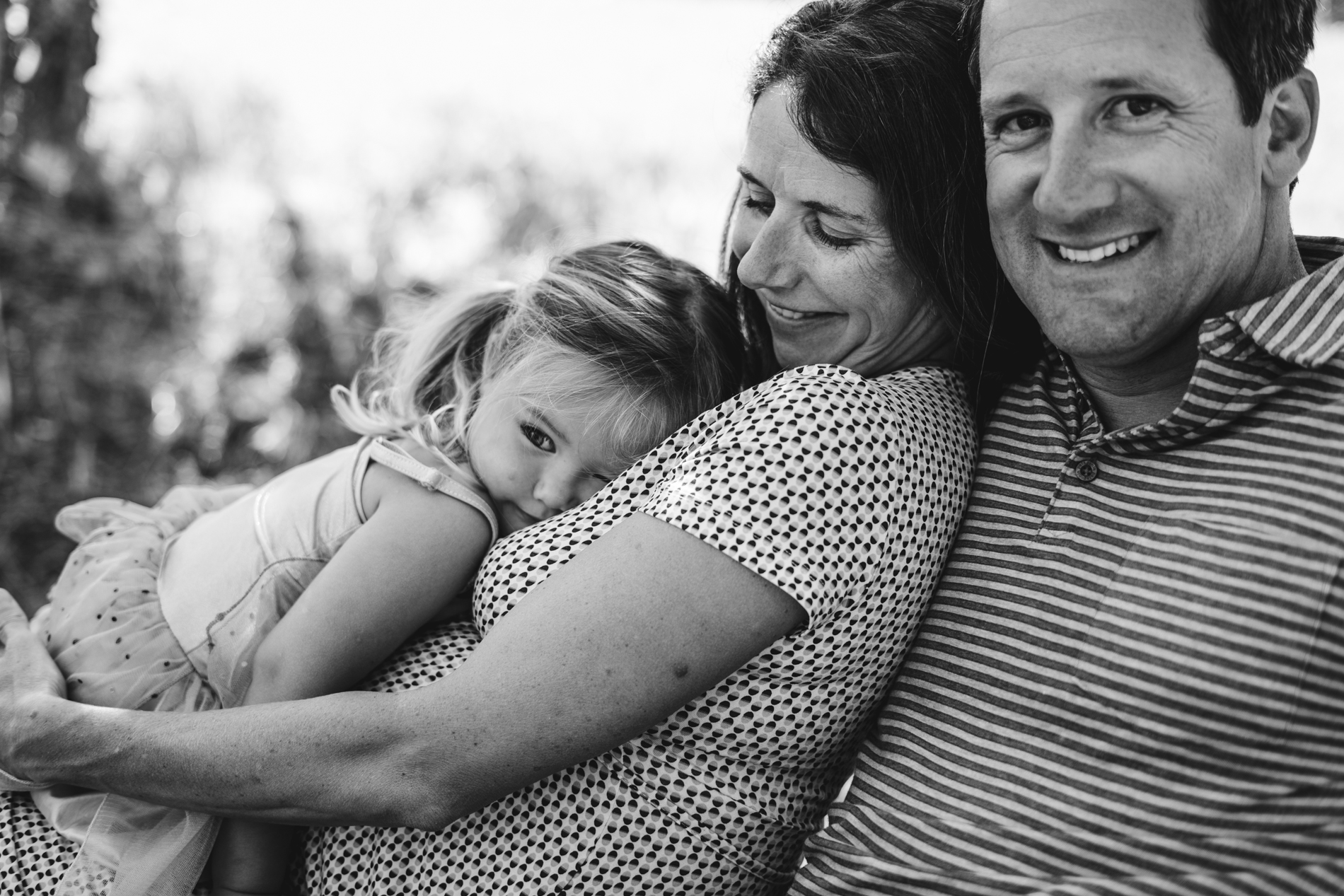 family cuddling under shade, daughter has head on moms chest