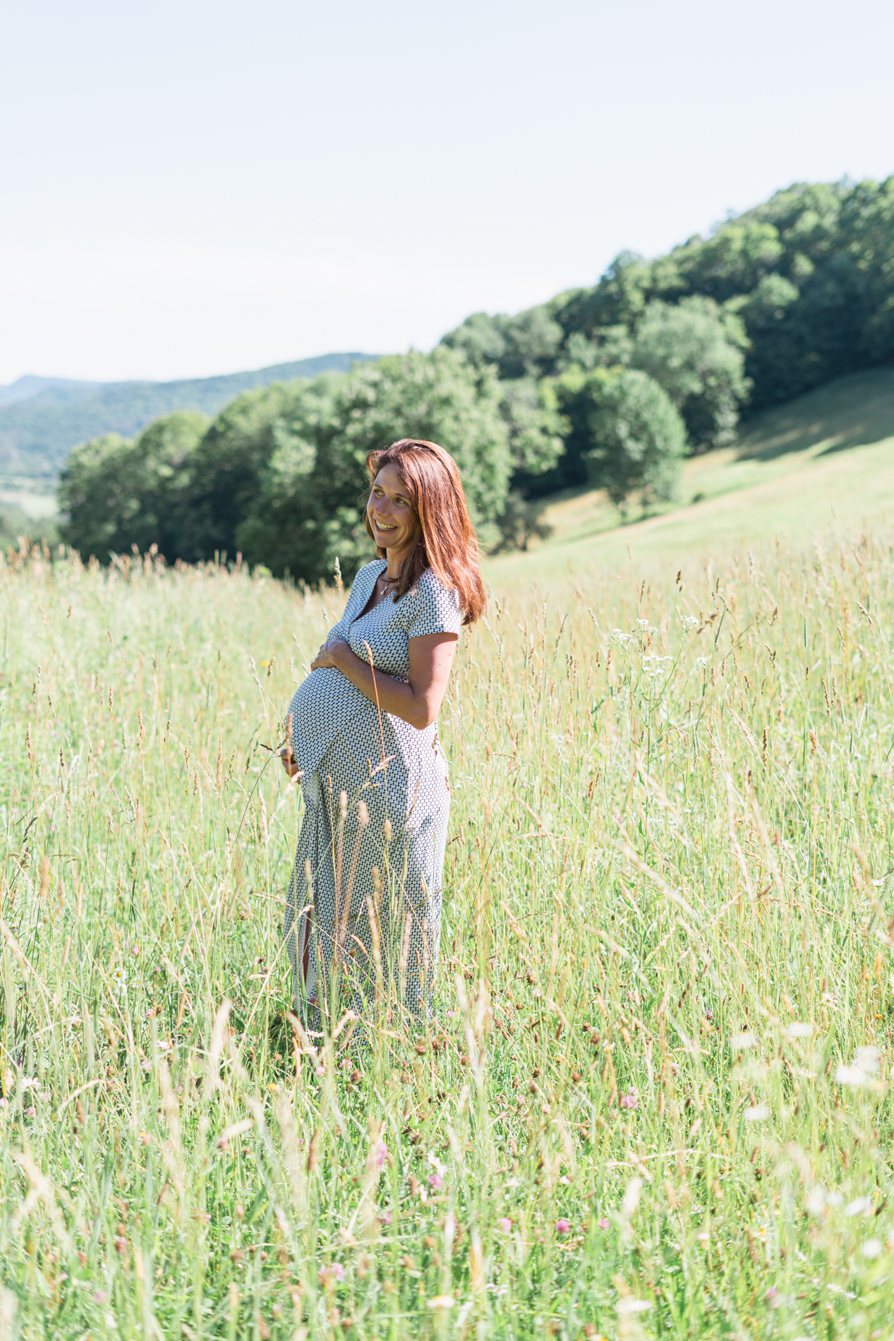 pregnant woman posing in field with vermont hillside in background, smiling