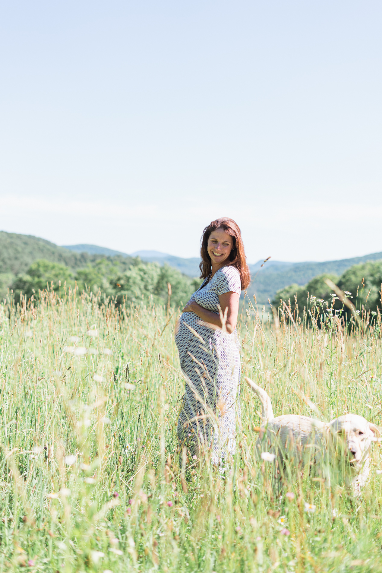 pregnant woman posing in field for maternity session with dog and vermont hills