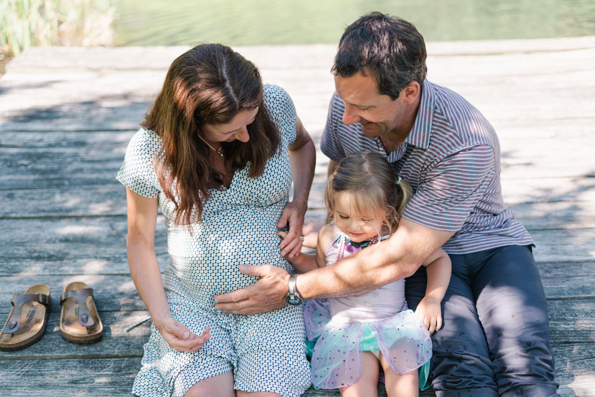 family with expecting mom sitting on doc under trees