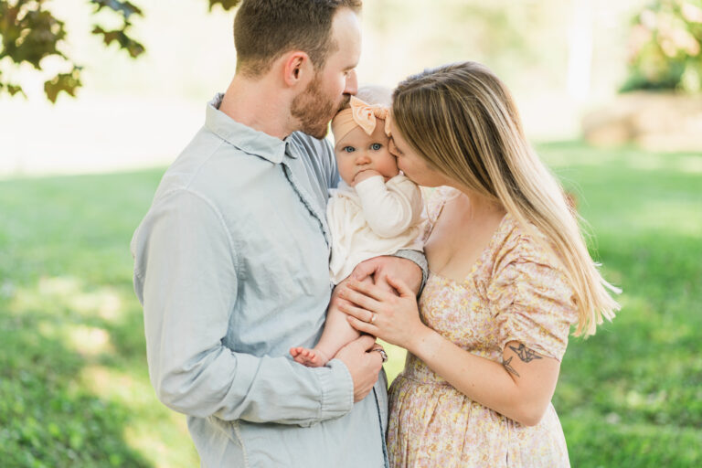 parents kissing baby with sunlit background