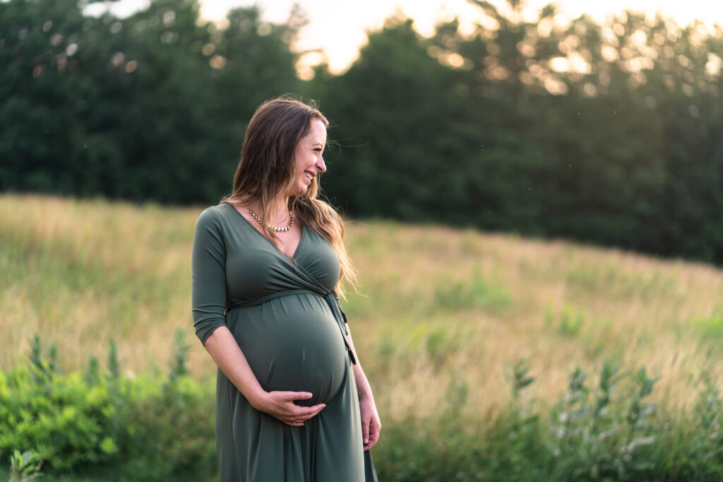 pregnant woman standing in field at sunseet