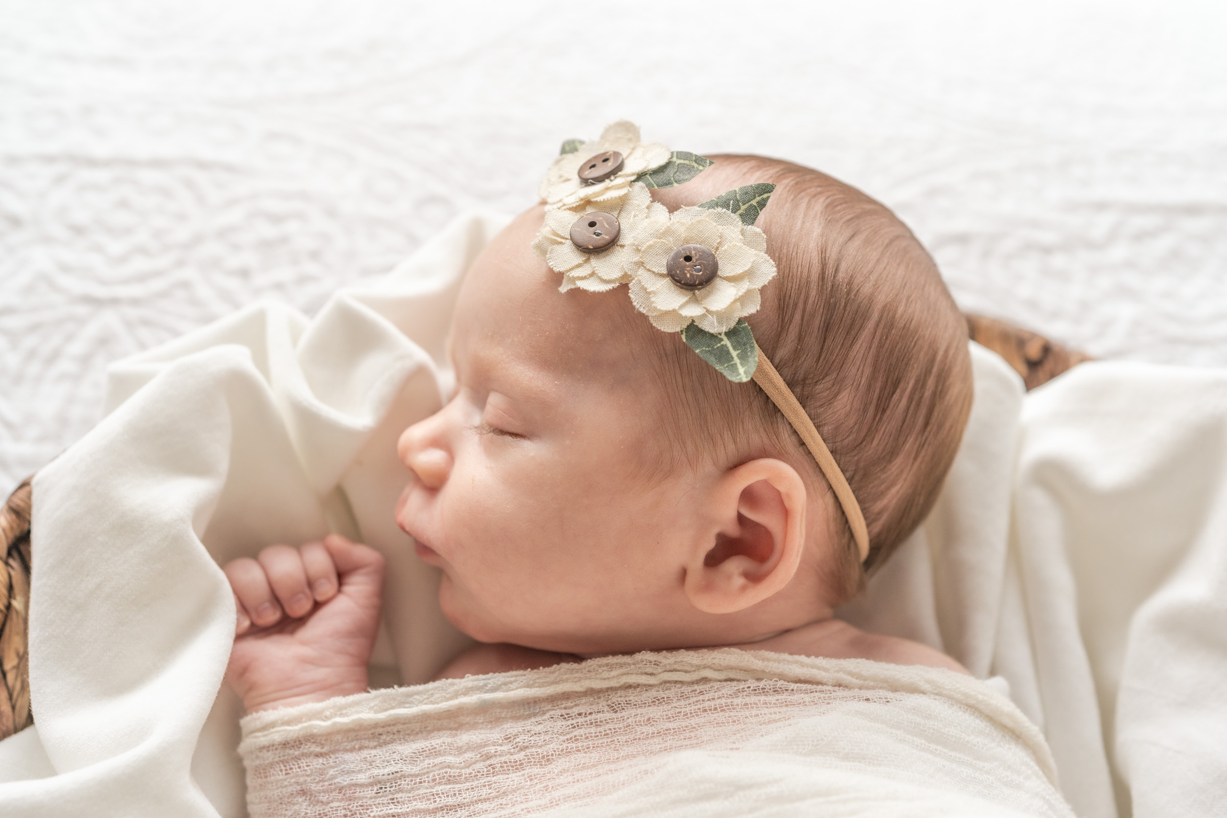 baby sleeping in basket with fabric, and white floral headband