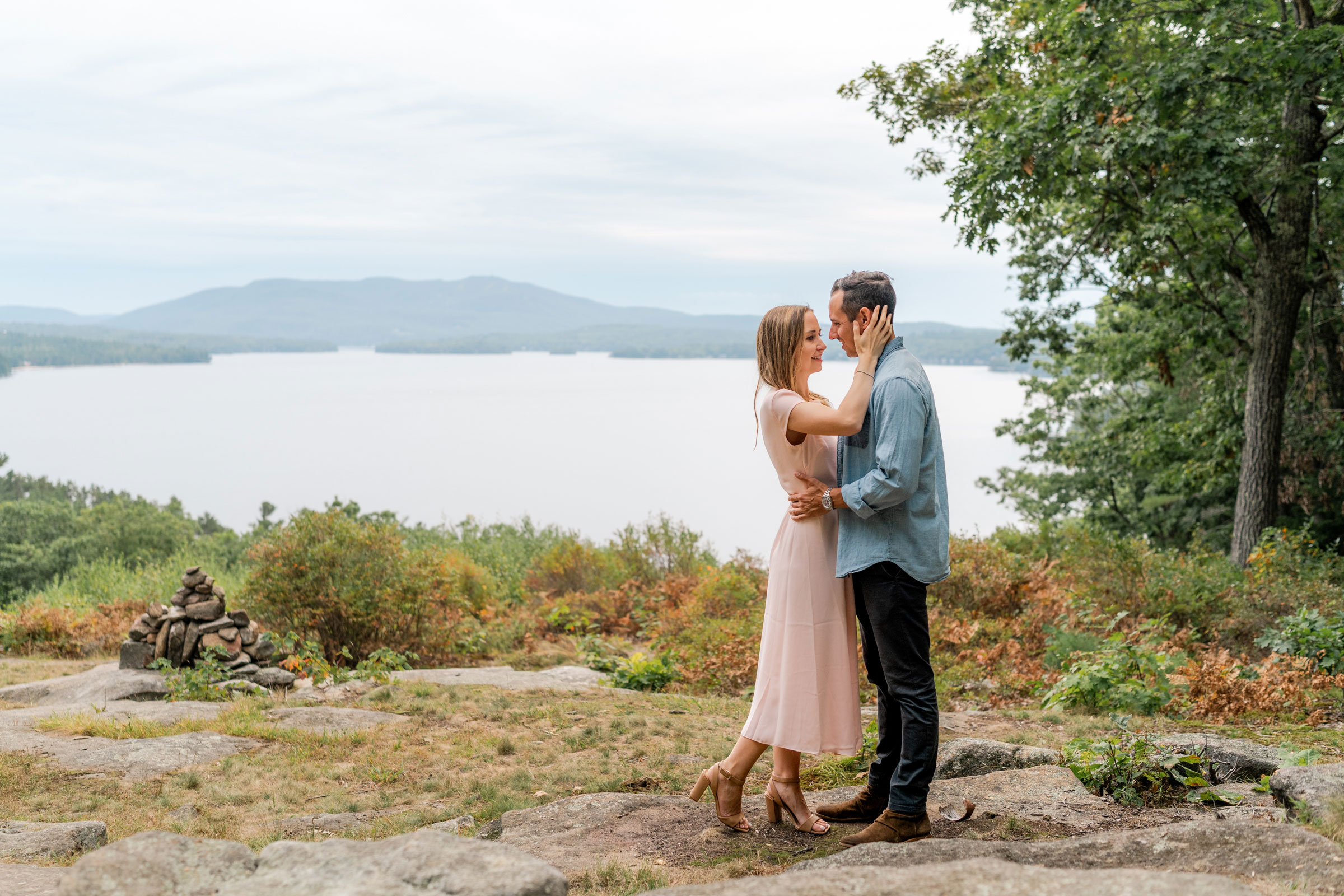 Couple posing with lake sunapee and mountains in background during lake sunapee engagement session