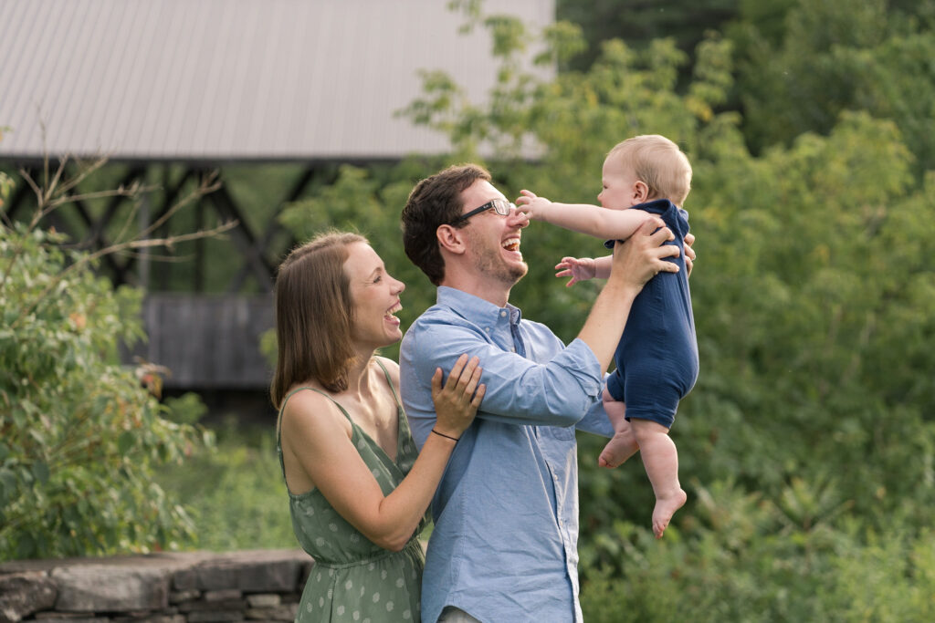 Couple holding child up in front of Packard Hill covered bridge, Lebanon