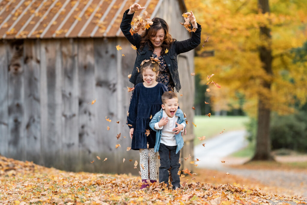 mother playfully sprinkling leaves over children during fall family photo session in the upper valley of NH and VT