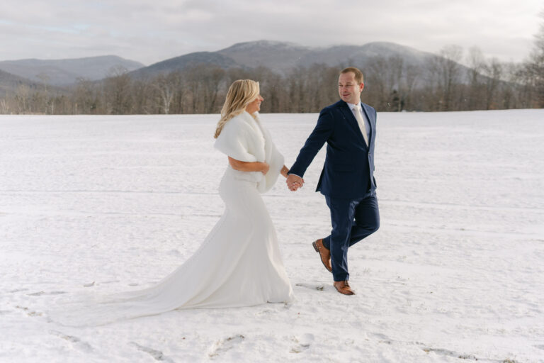 Couple walking across snowy landscape with mountains in background