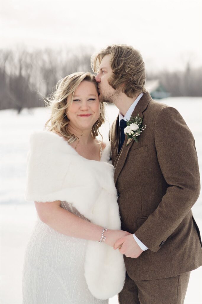 groom kissing brides head during winter first look at mountain top inn, chittenden, vt