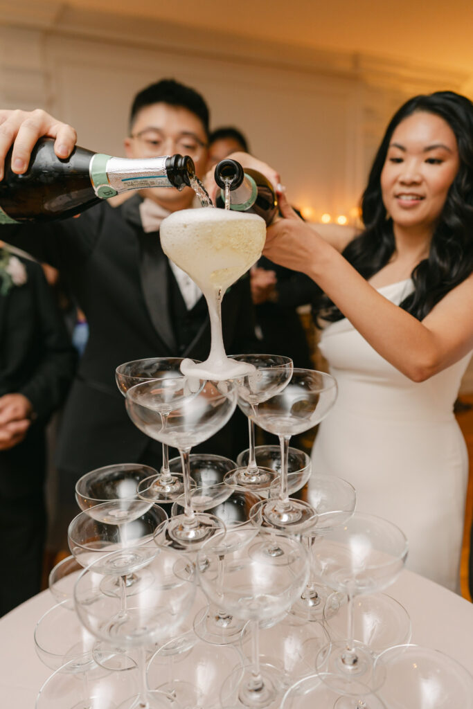 couple pours champagne tower during cocktail hour