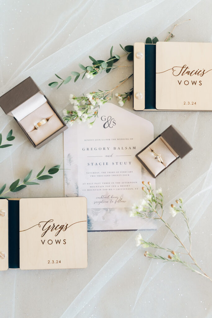 wide shot of stationary flatlay and rings with florals and wooden vowbooks