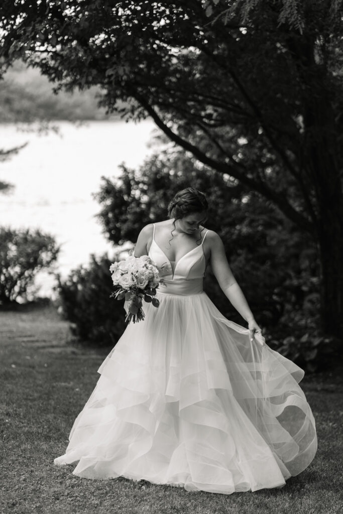 bride standing in dress with dark woods behind her and lake in the distance