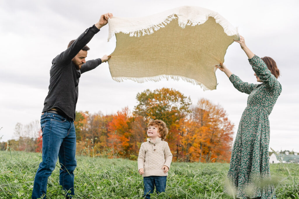 parents flying a blanket over the head of their son during fall family photo session