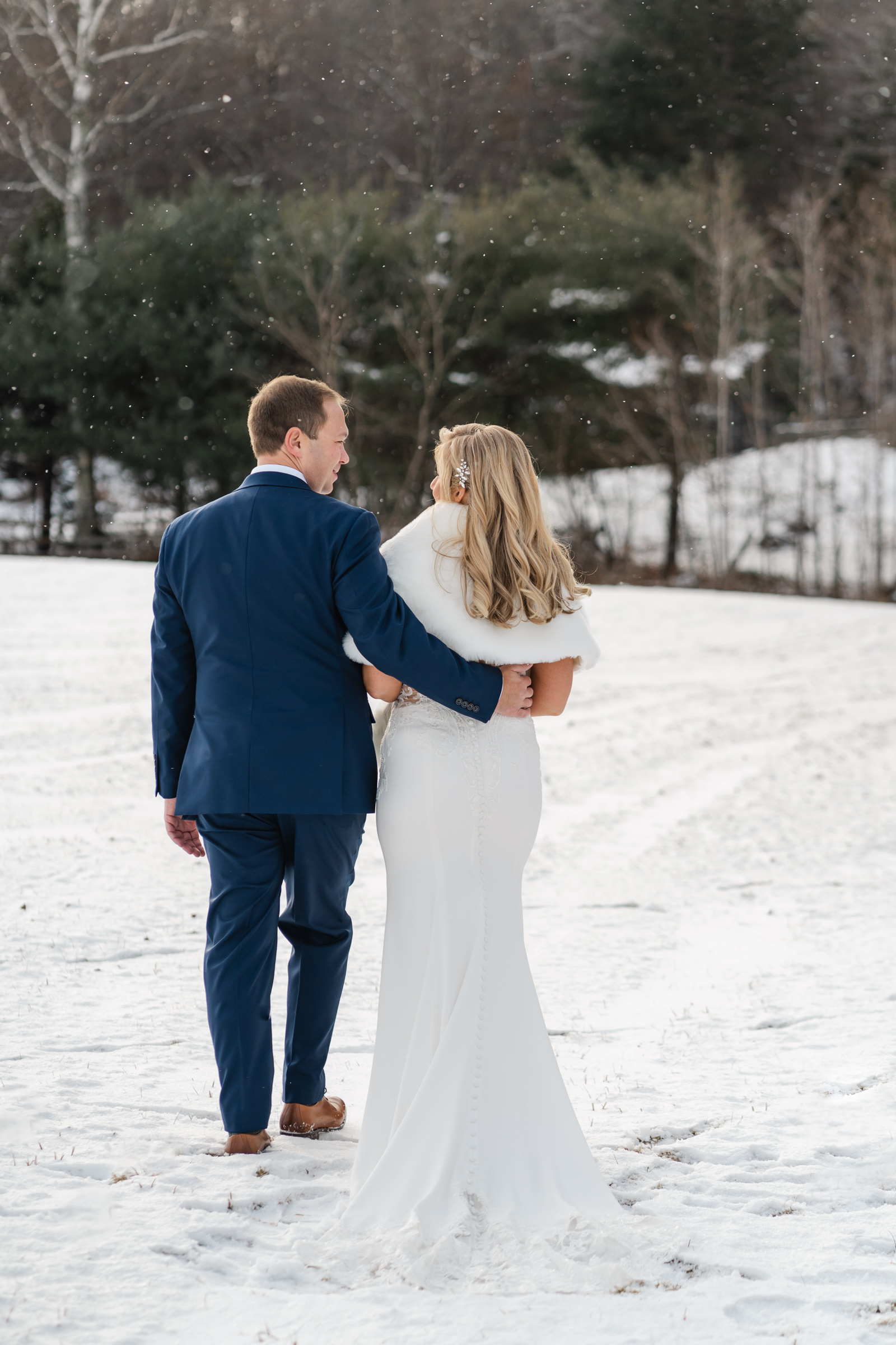 groom in blue suit wraps arm around bride during first look