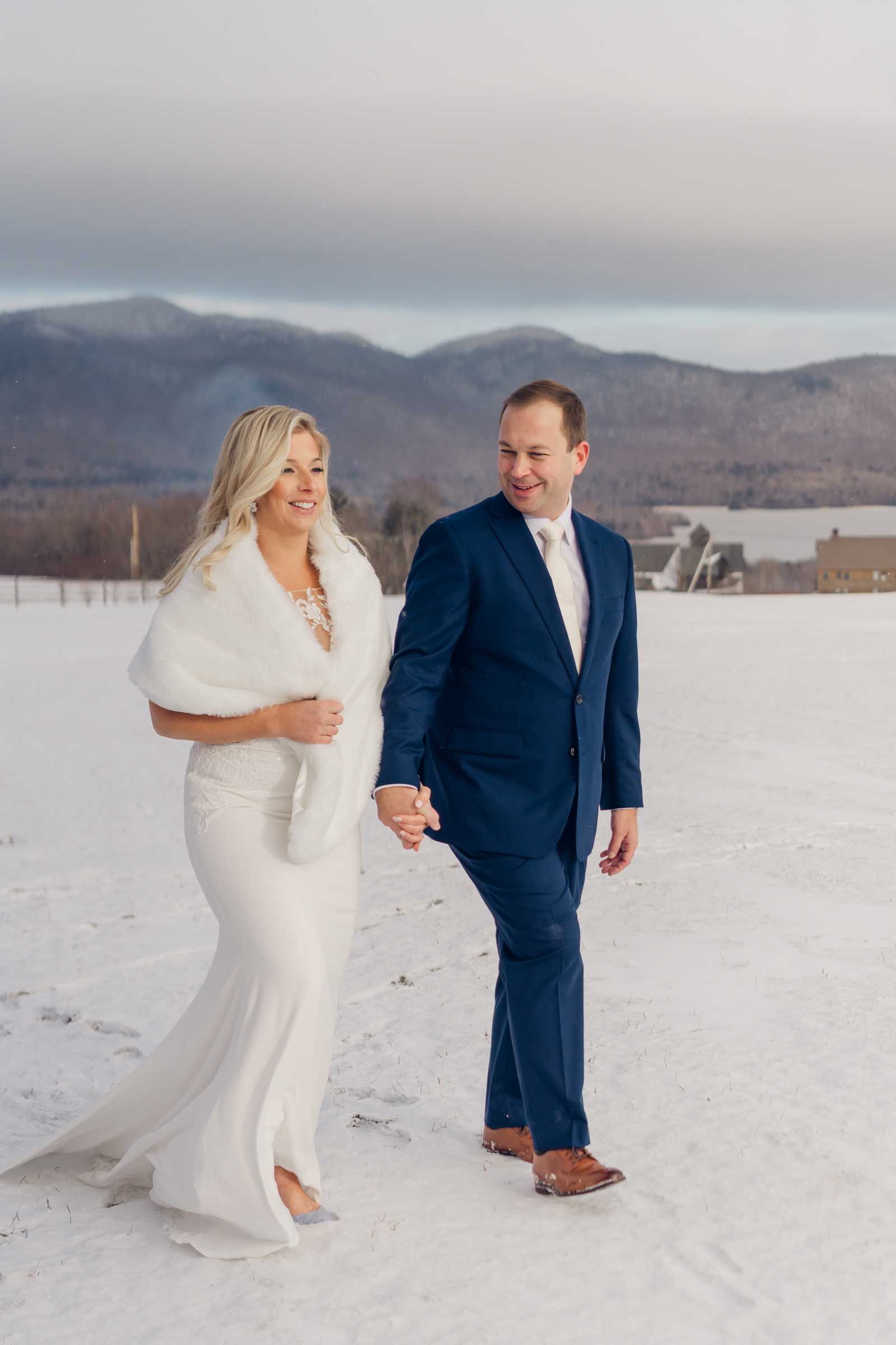 beautiful warm light washes over couple as they walk across snow covered field during winter wedding at mountain top resort