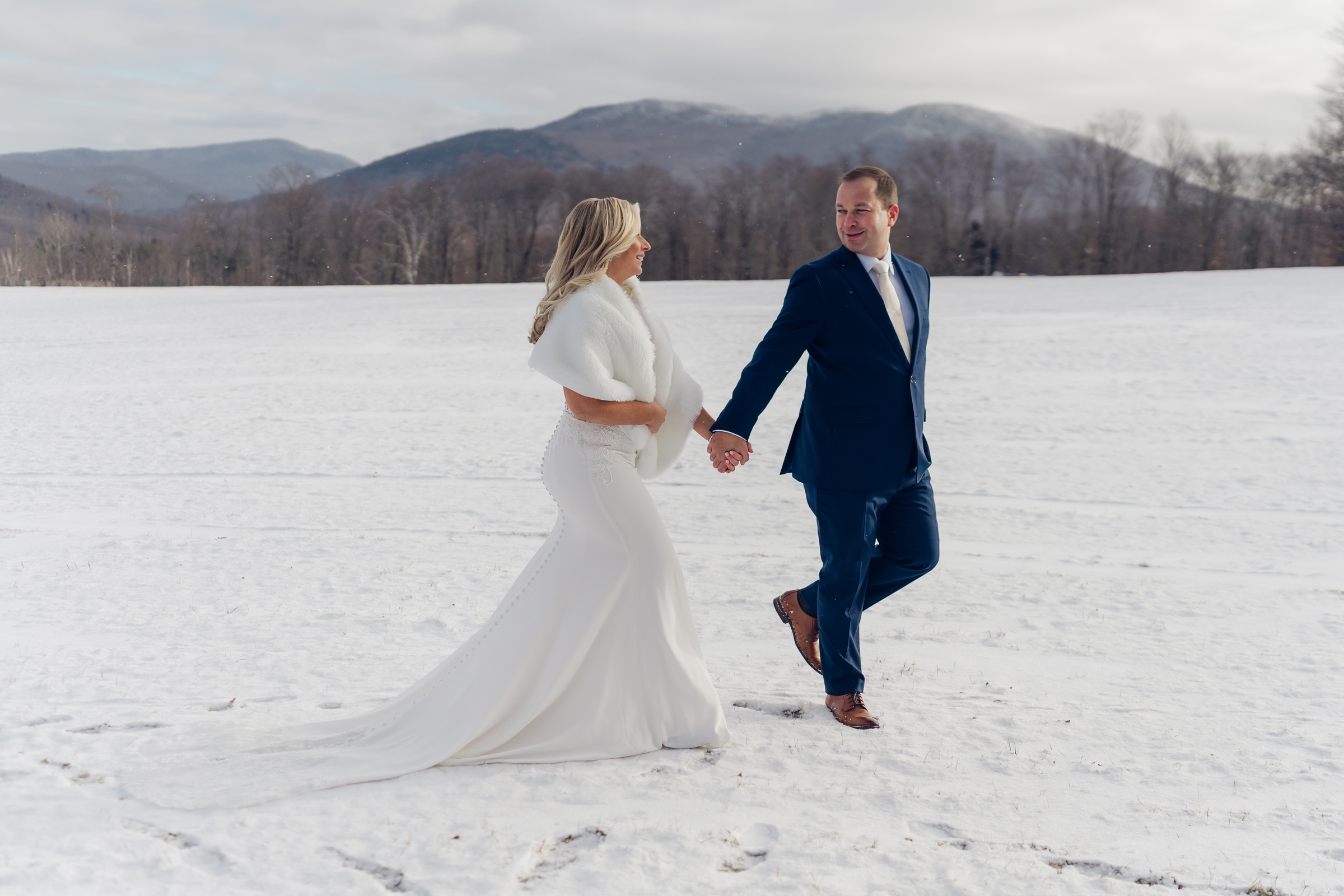 Couple walking across snowy landscape with mountains in background