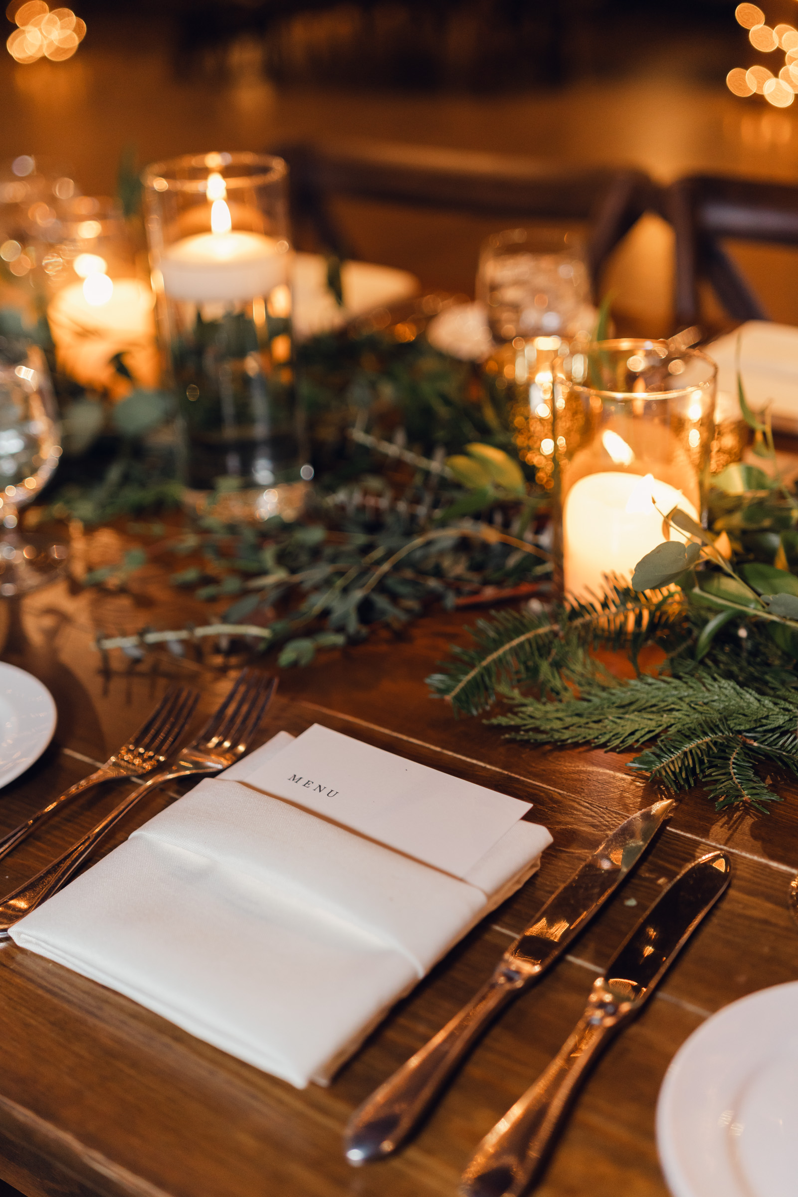 place setting surrounded by greenery and gold candles