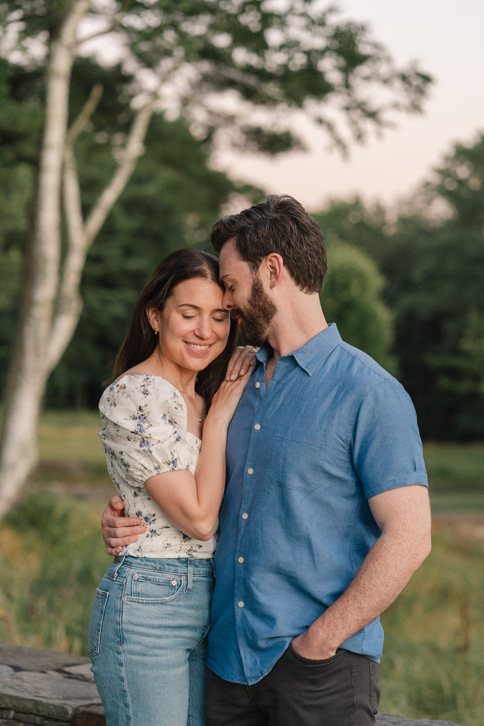 sunset engagement session in vermont, woman leans on man's shoulder