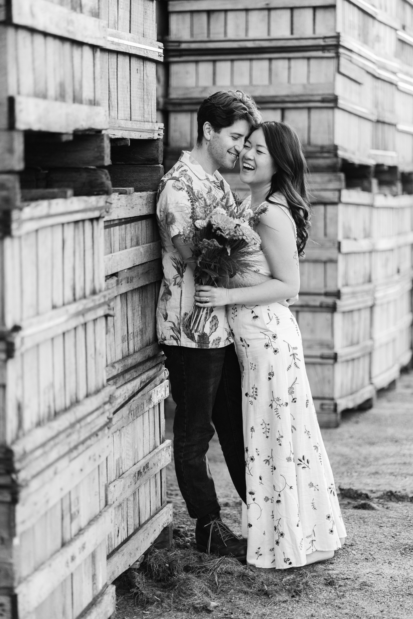 couple snuggling near apple crates during upper valley engagement session at poverty lane orchards