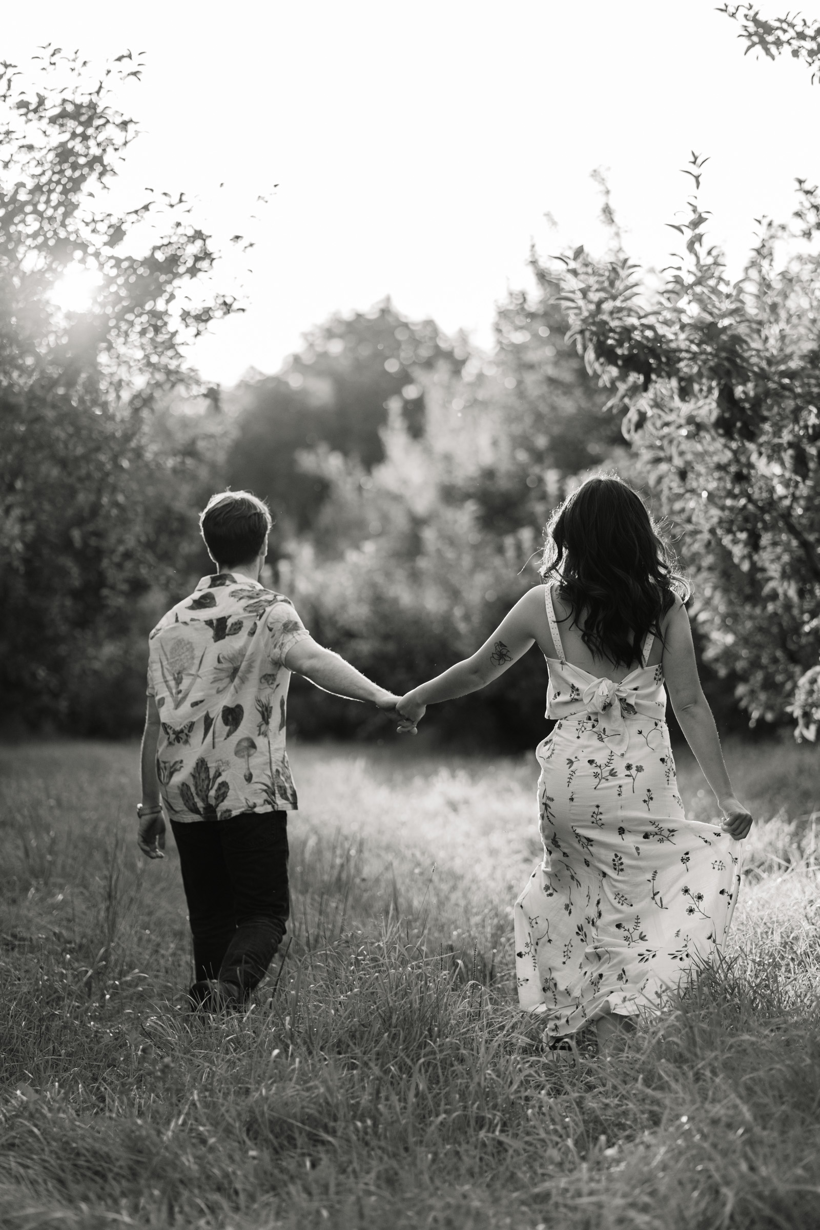 couple walk through grass, ethereal light during upper valley engagement session at poverty lane orchards