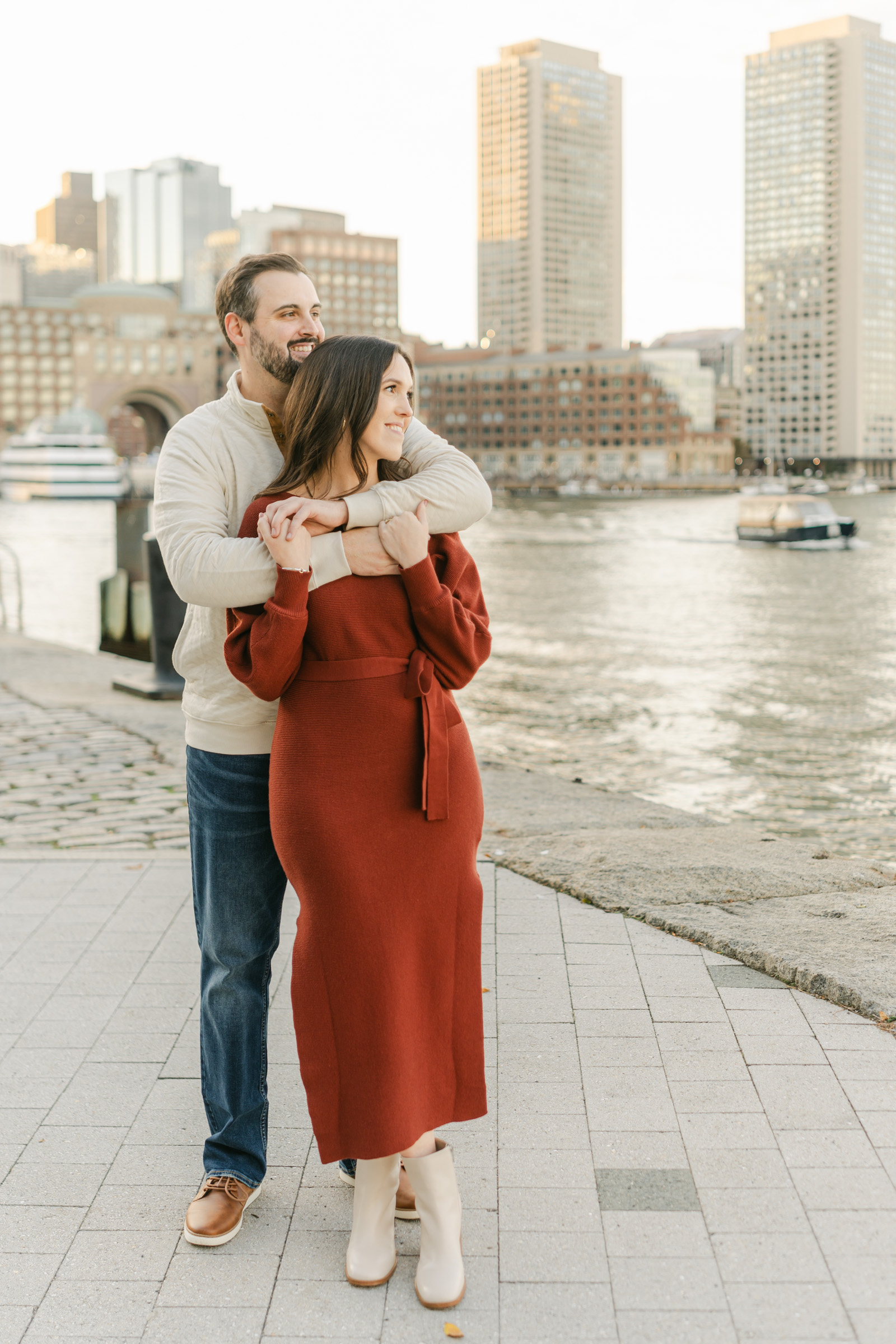 couple snuggling and looking out at water during boston waterfront engagement session