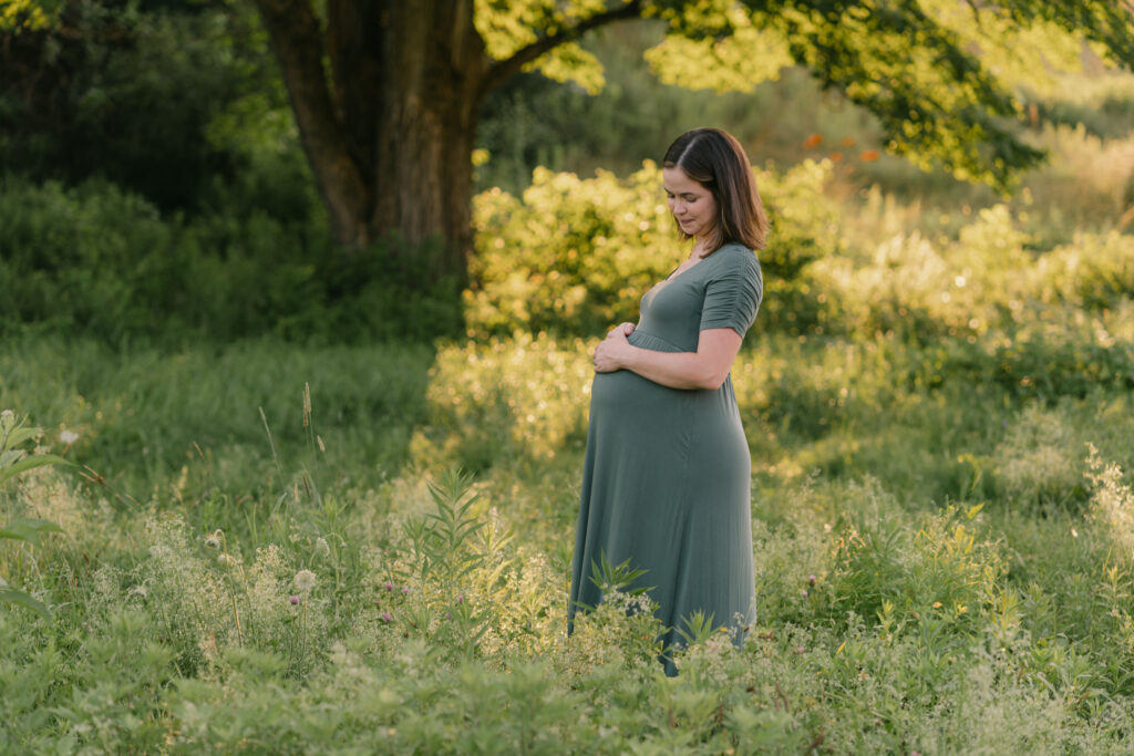 beautiful expecting mother standing in grass under a tree