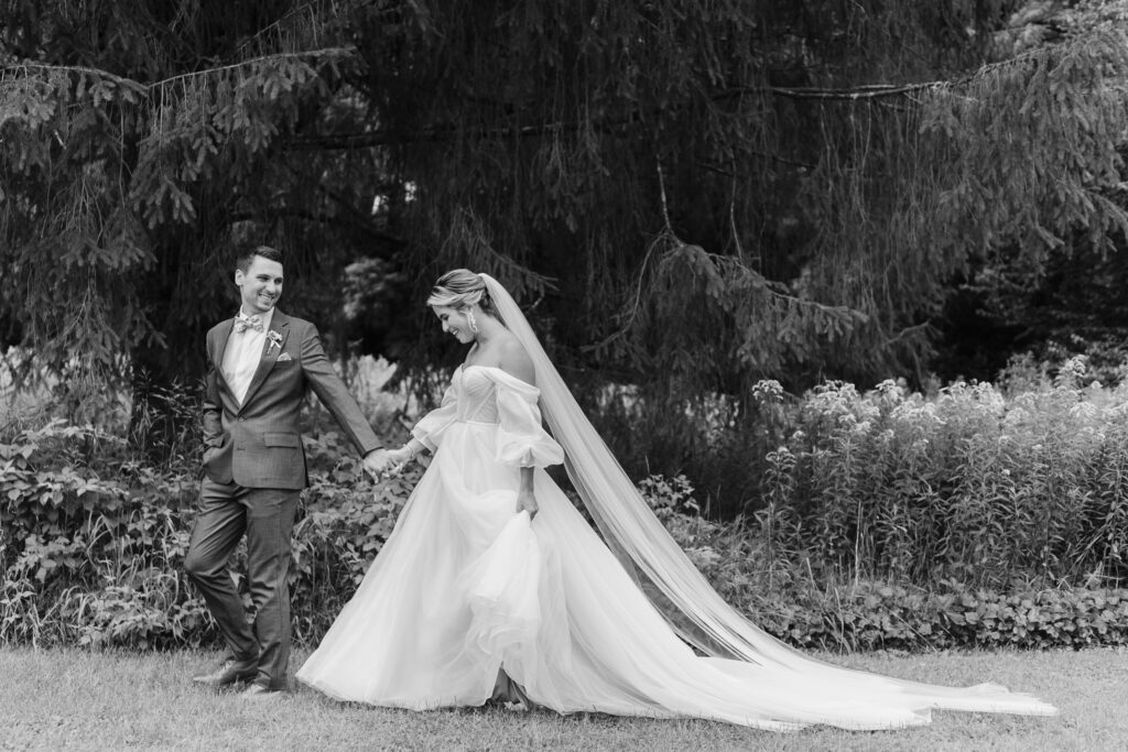 bride and groom walking across field in wedding attire at quechee inn in quechee vt