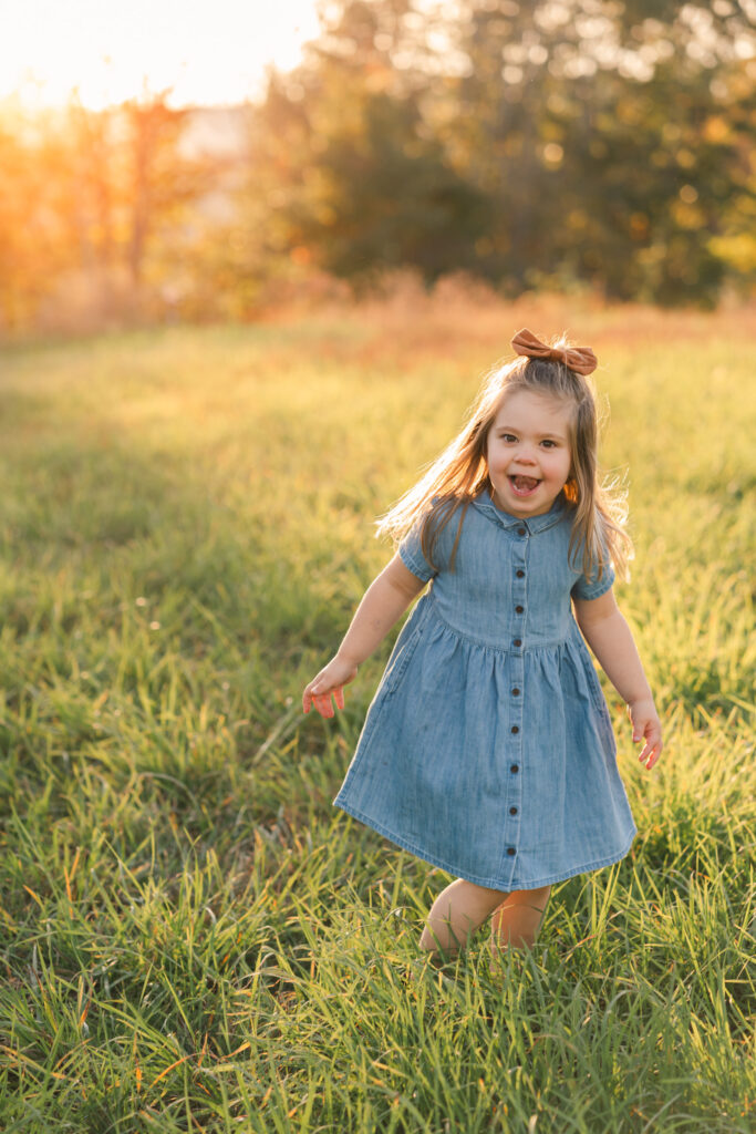 little girl in denim dress running through field during upper valley fall family photo session