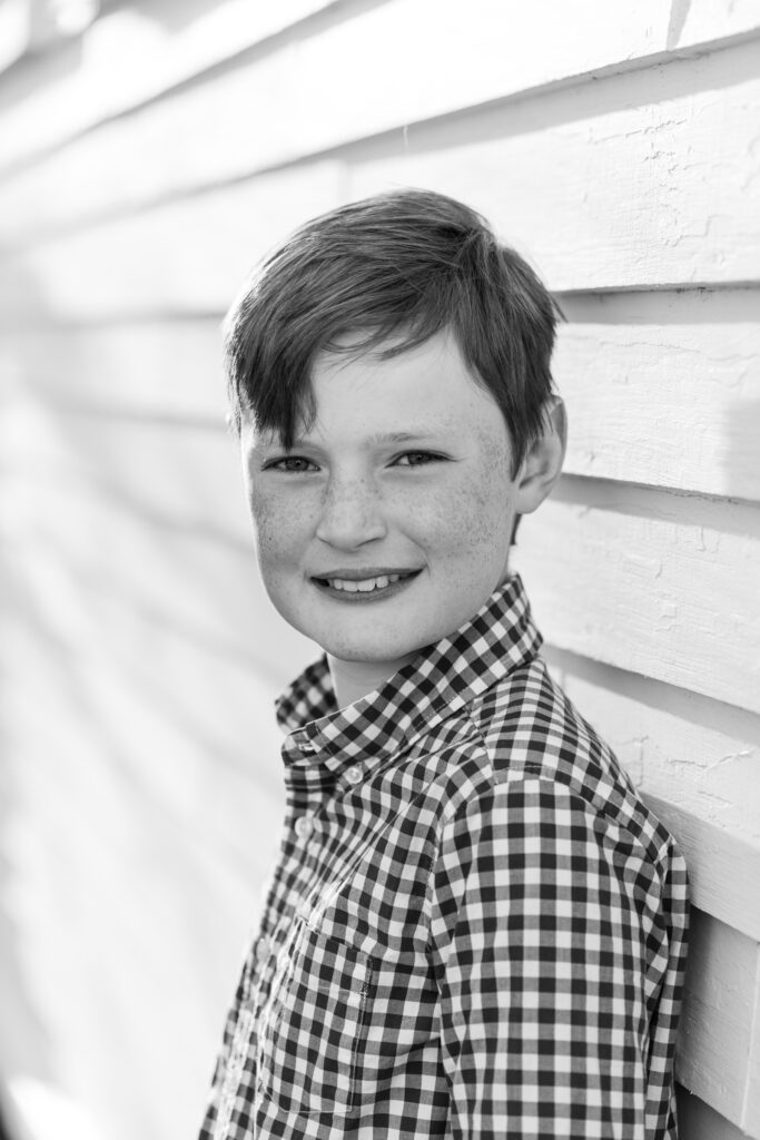 portrait of young boy against white wooden barn