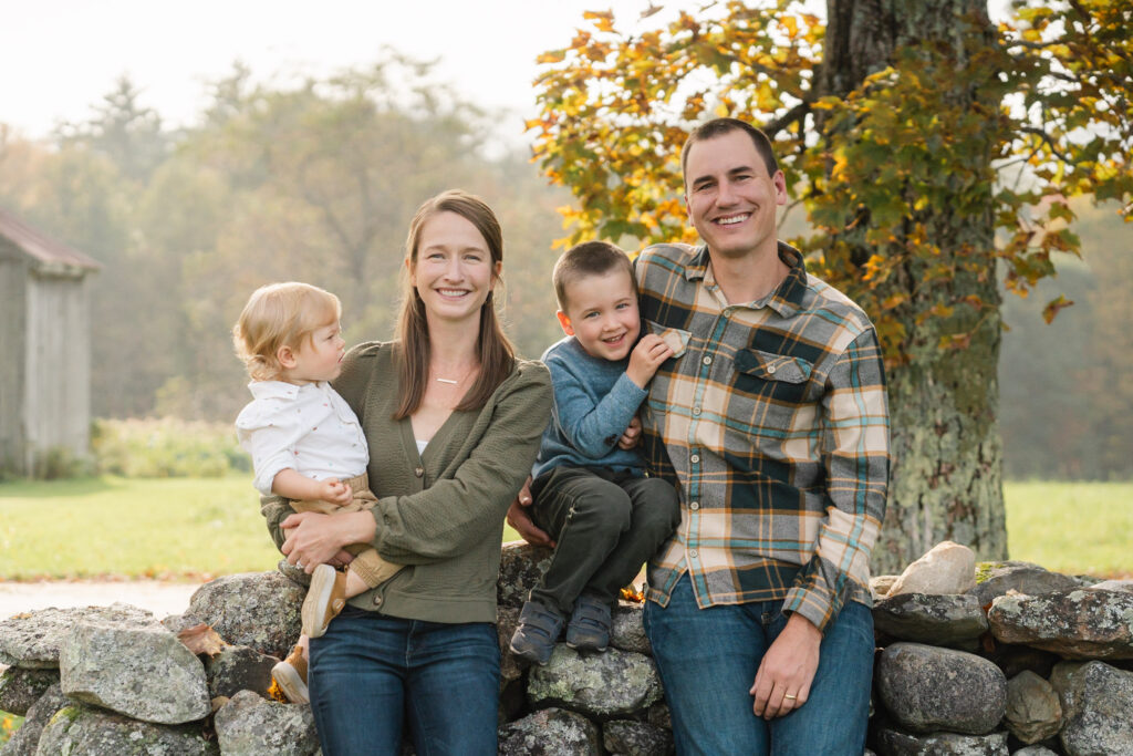 family sitting on stone wall at musterfield farm, upper valley family photographer