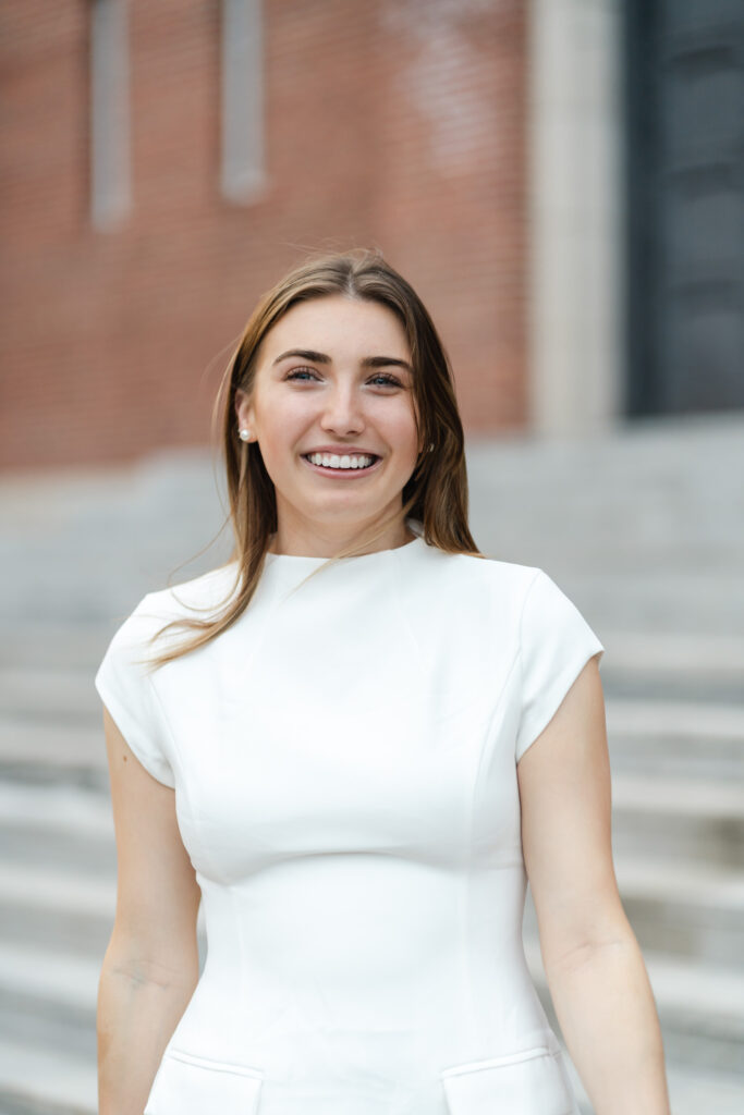 candid, free close-up portrait of woman in white dress on steps of armory during norwich university grad session