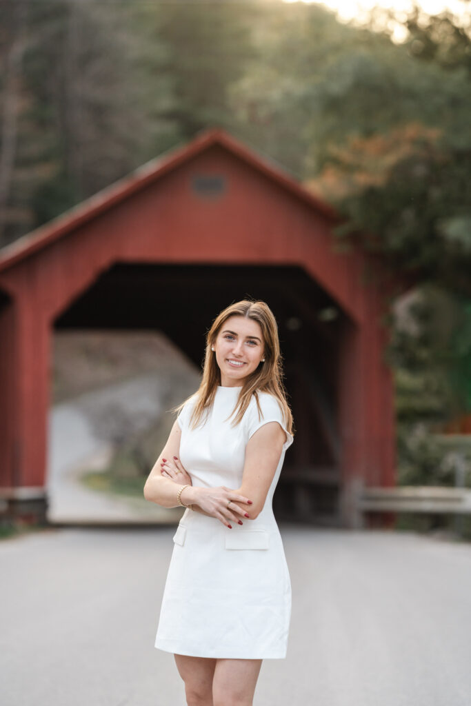 female in white dress posing in front of northfield vermont covered bridge, mid-length portrait