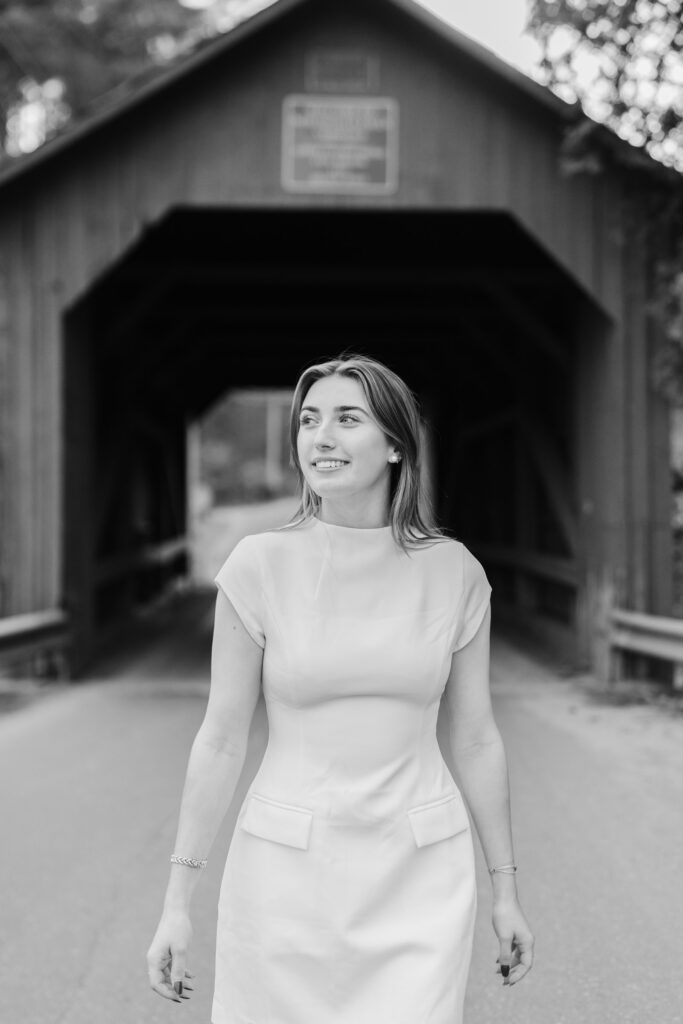 female in white dress walking away from northfield vermont covered bridge, mid-length portrait looking off to distance