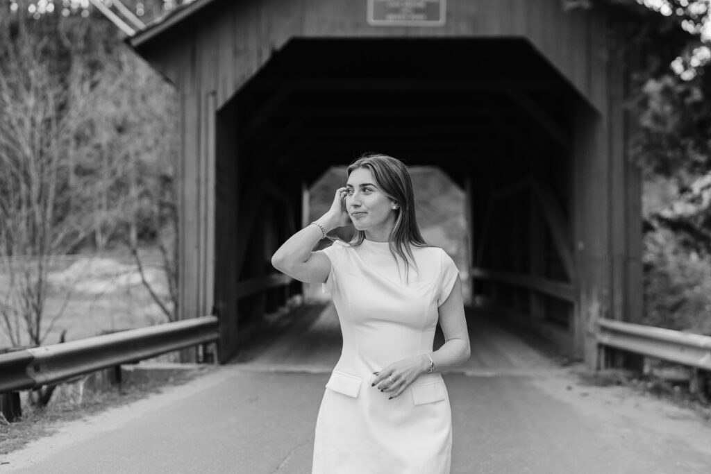 female in white dress walking away from northfield vermont covered bridge, brushing hair back