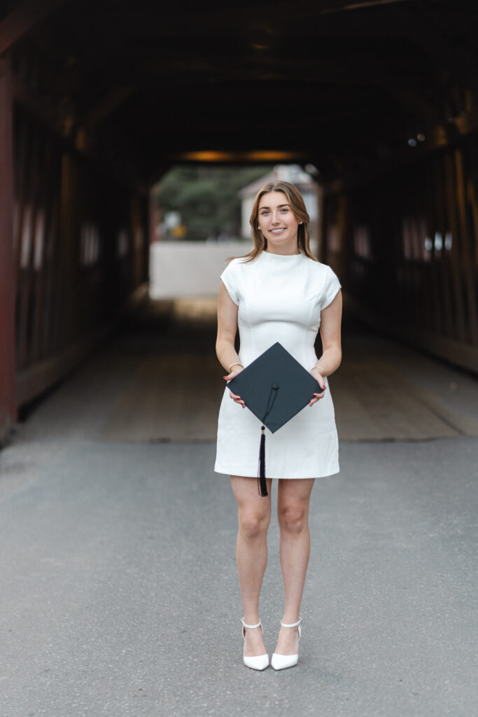 female in white dress walking away from northfield vermont covered bridge, holding cap in hands